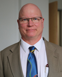 headshot of white bald man wearing eyeglasses