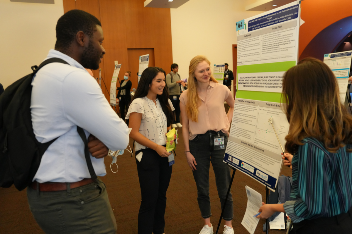 Four students standing in front of a poster on display in a conference room.