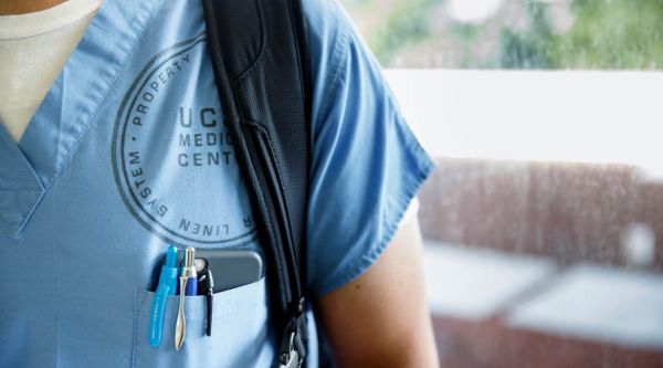 Image of residents left shoulder with writing pens and a cell phone in the chest pocket 