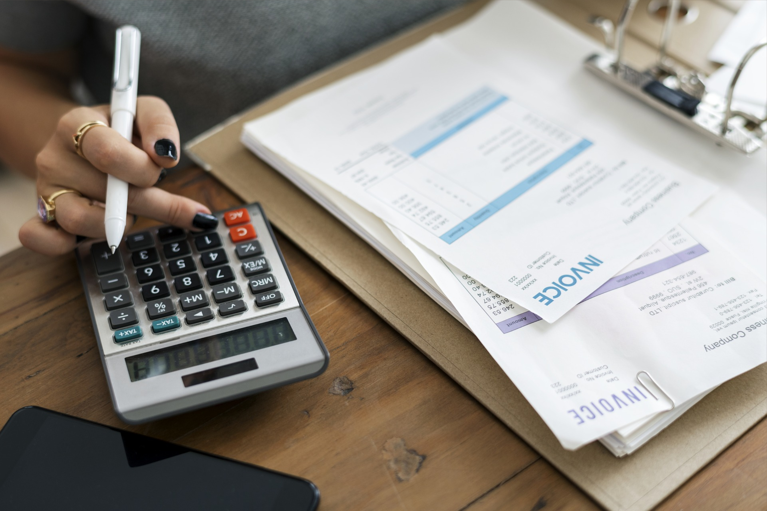 an image showing a hand on a calculator with invoice papers