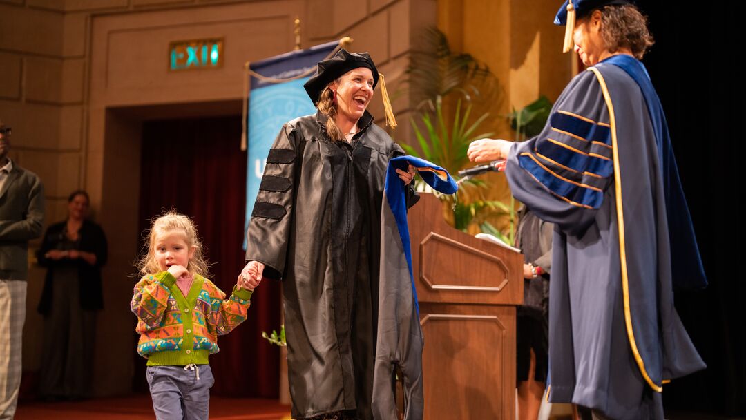 woman holding a child's hand and receiving her diploma