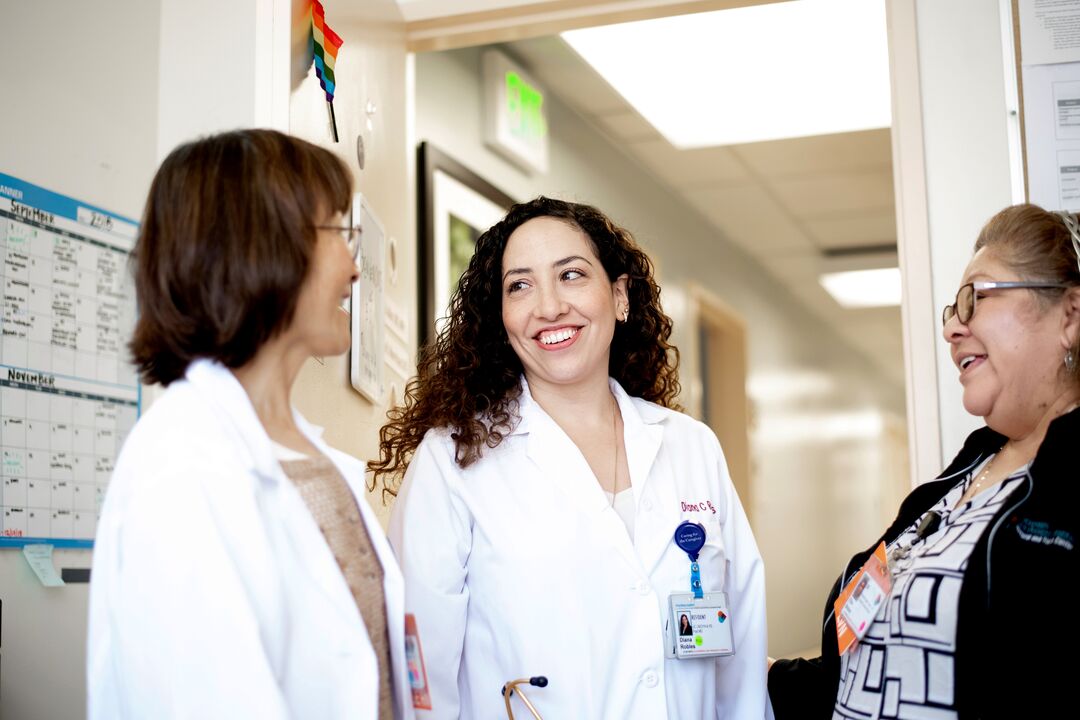 three people standing, smiling and talking